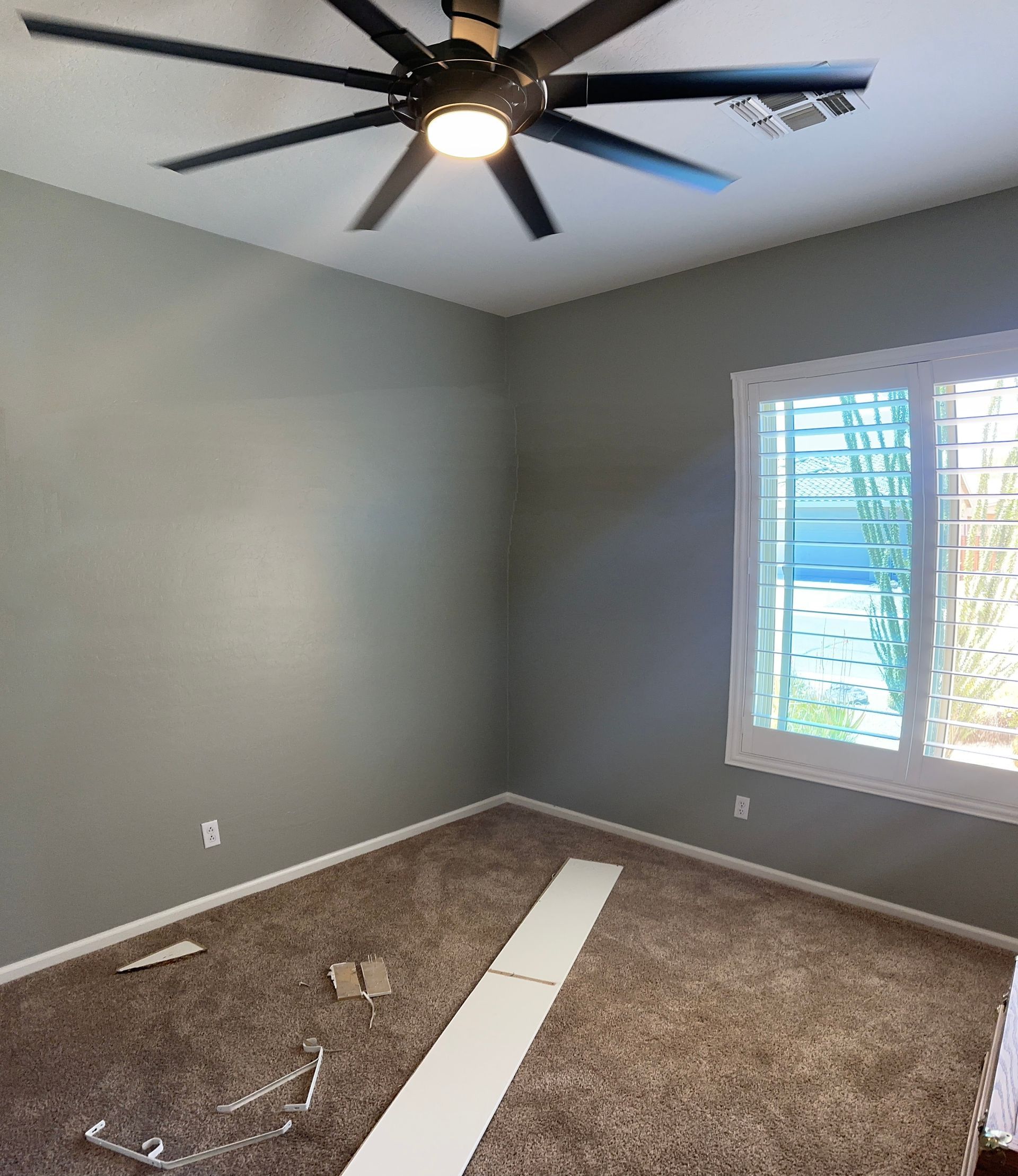 Empty gray bedroom with ceiling fan, window blinds, and carpet pieces on the floor