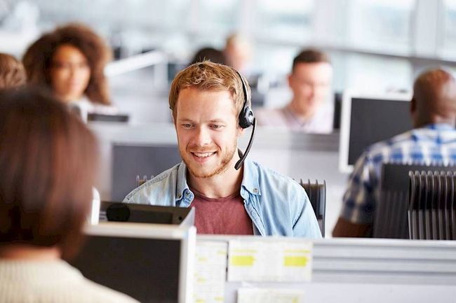 A man wearing a headset is sitting in front of a computer in a call center.