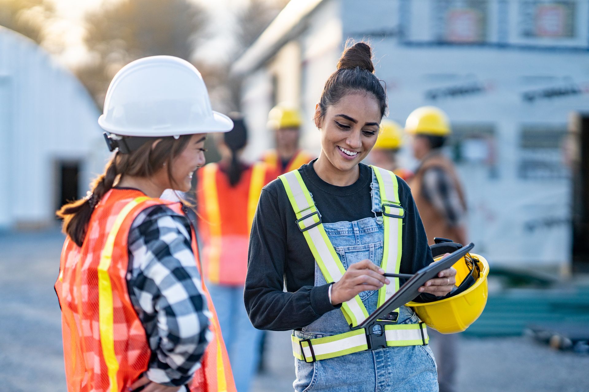 Construction workers reviewing a tablet on a building site. Smiling woman points at screen.