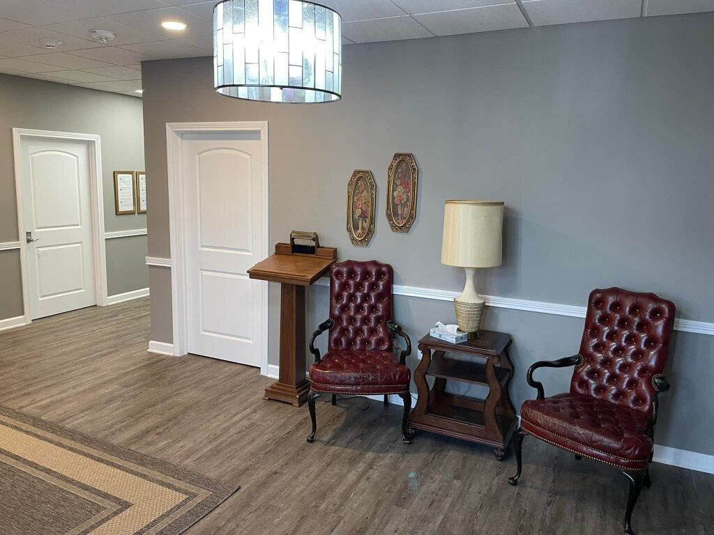 Carpeted lobby with gray walls, white doors, red chairs, side table, lamp, and hanging light fixture.