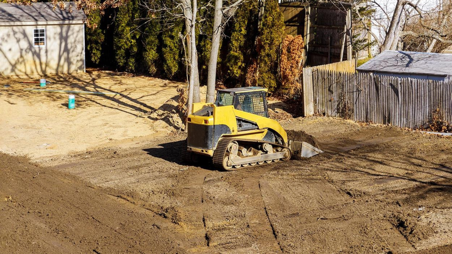 Yellow mini excavator leveling dirt in a backyard construction site