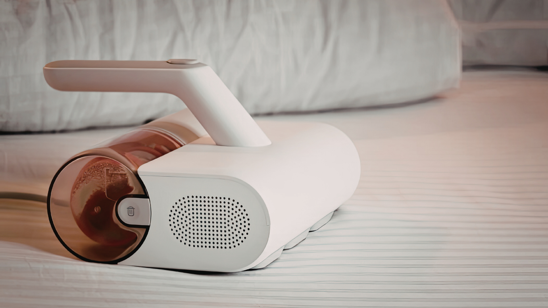 Portable white-and-rose speaker lying on a bed beside a copper tumbler.