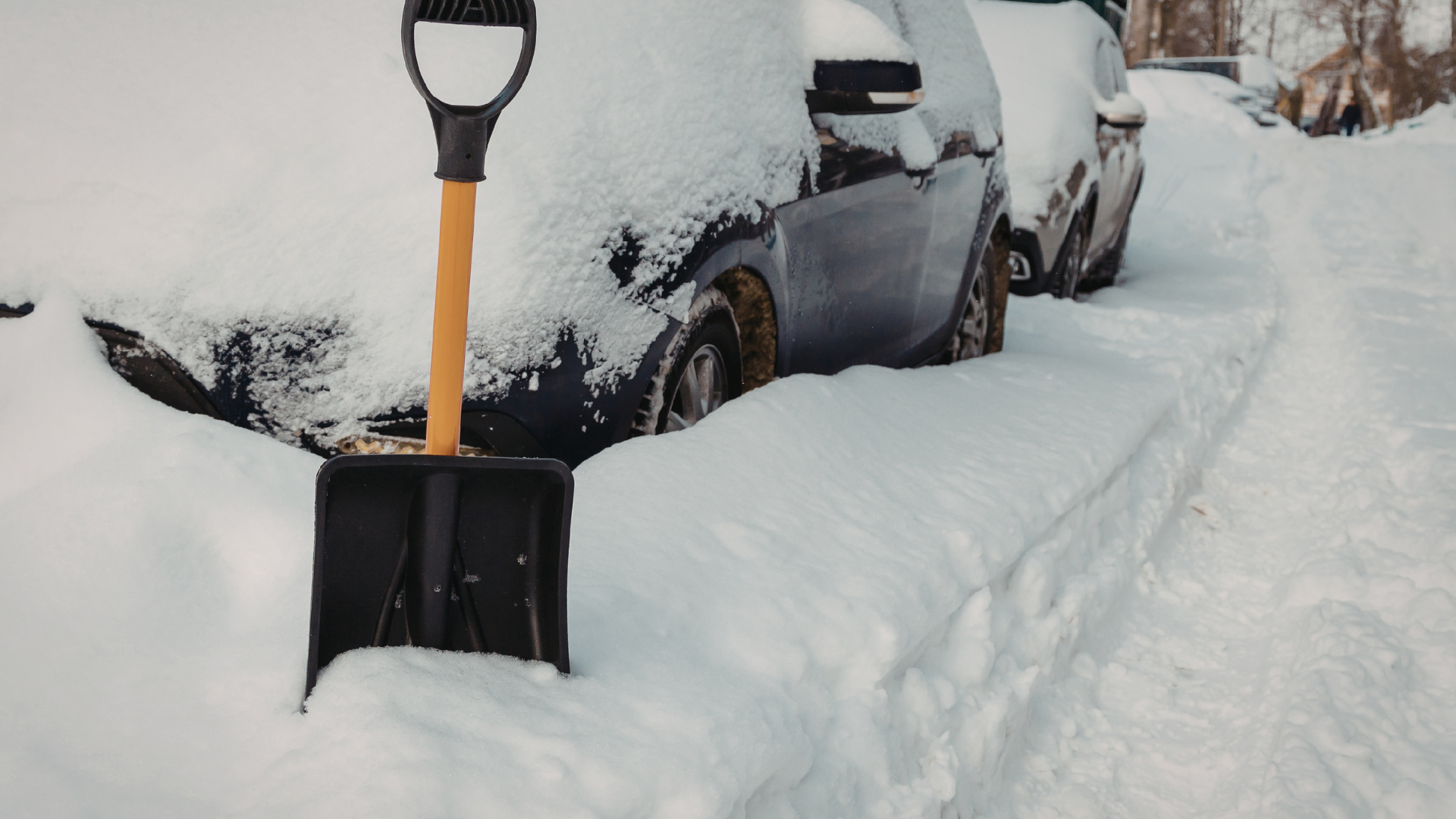 Snow-covered parked cars with a black-and-orange shovel stuck in a deep snowbank