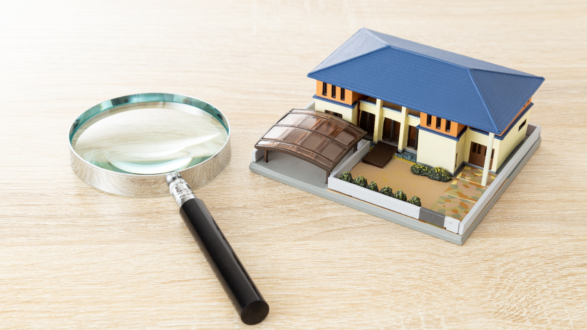 Magnifying glass beside a small house model on a wooden surface