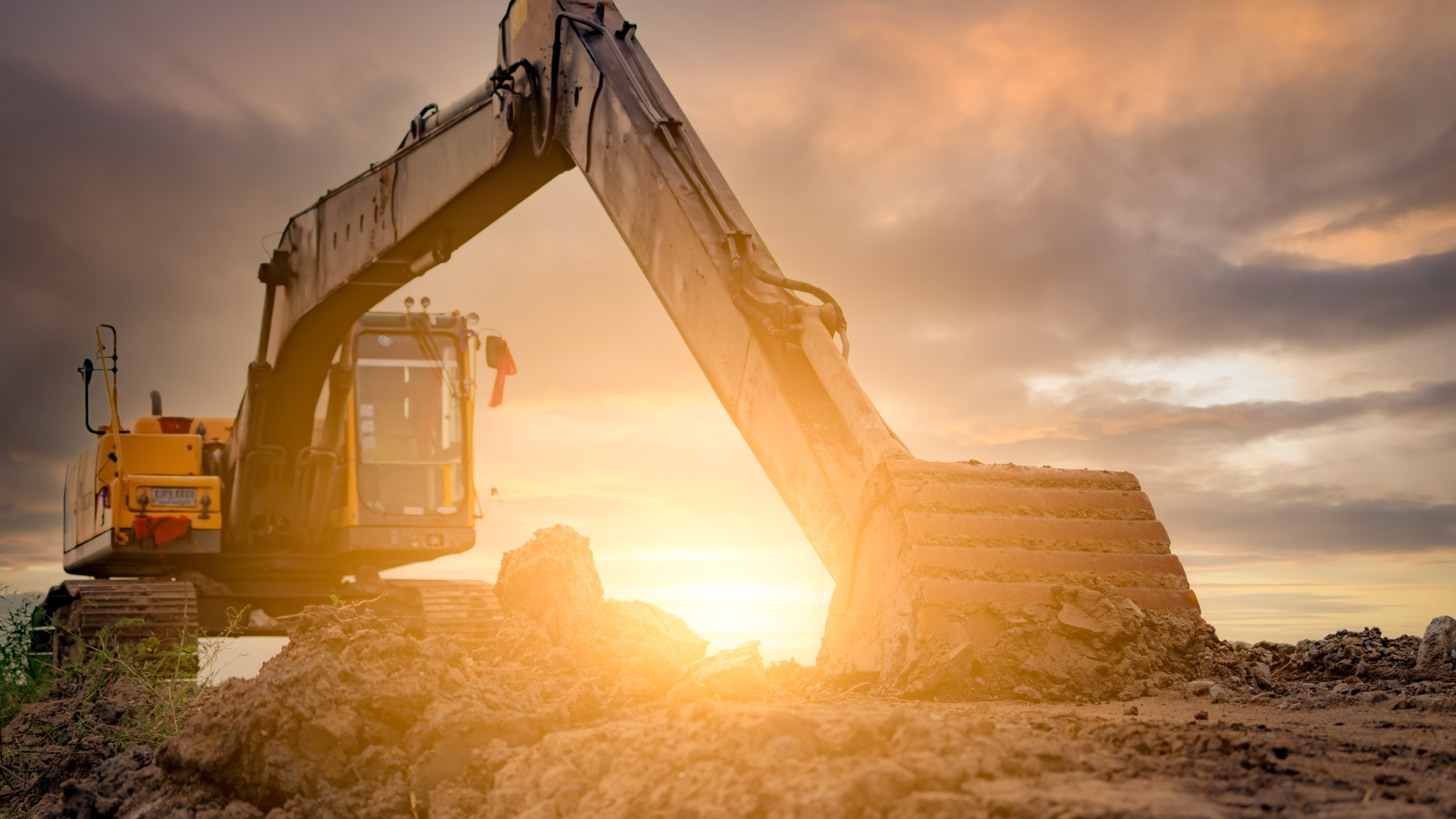 An excavator is working on a construction site at sunset.