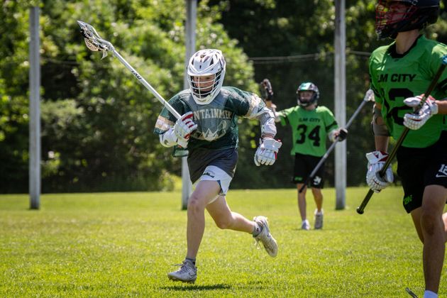 Lacrosse players in green jerseys run across a sunny field during a game