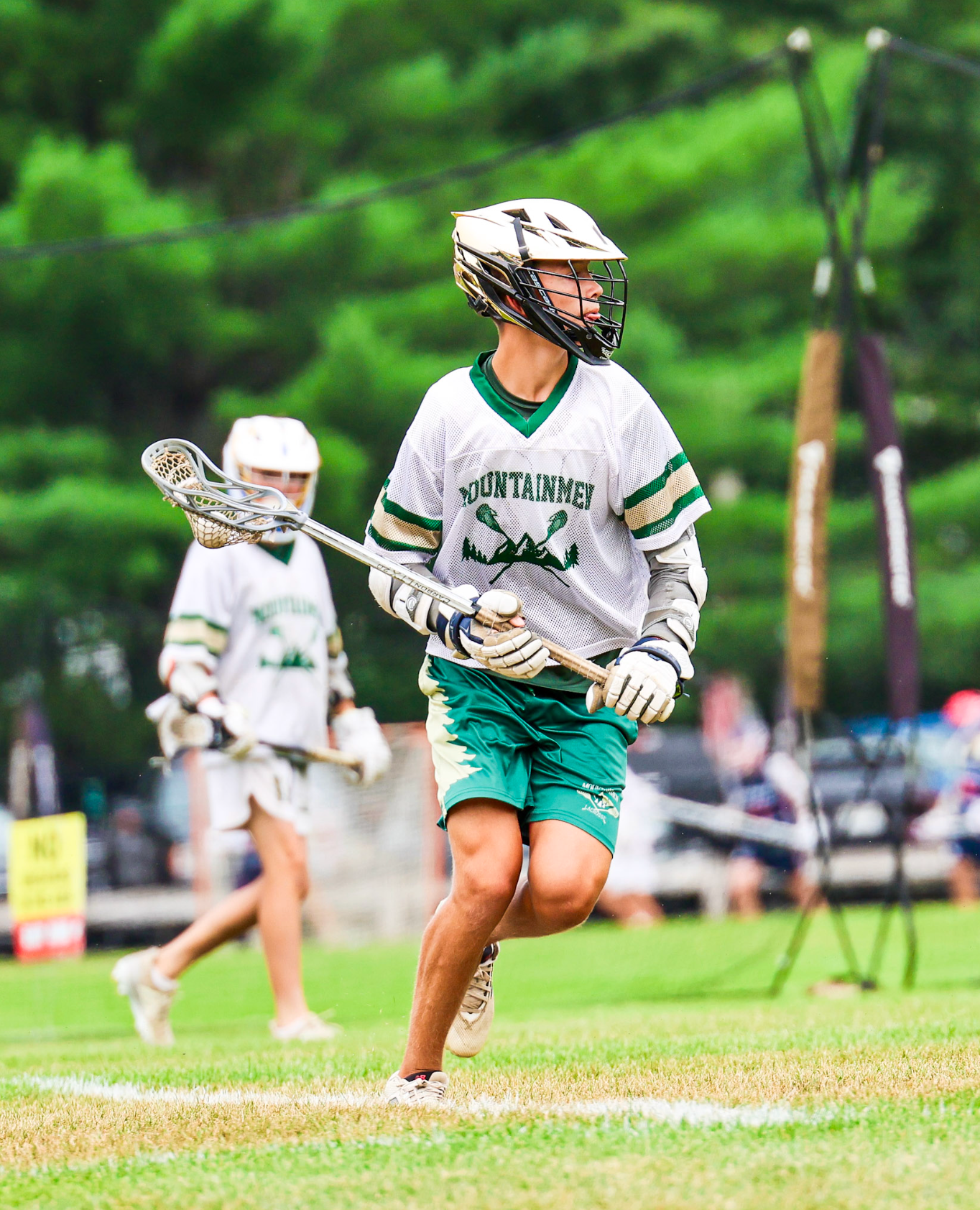 Lacrosse player in white and green uniform runs on a grassy field holding a stick