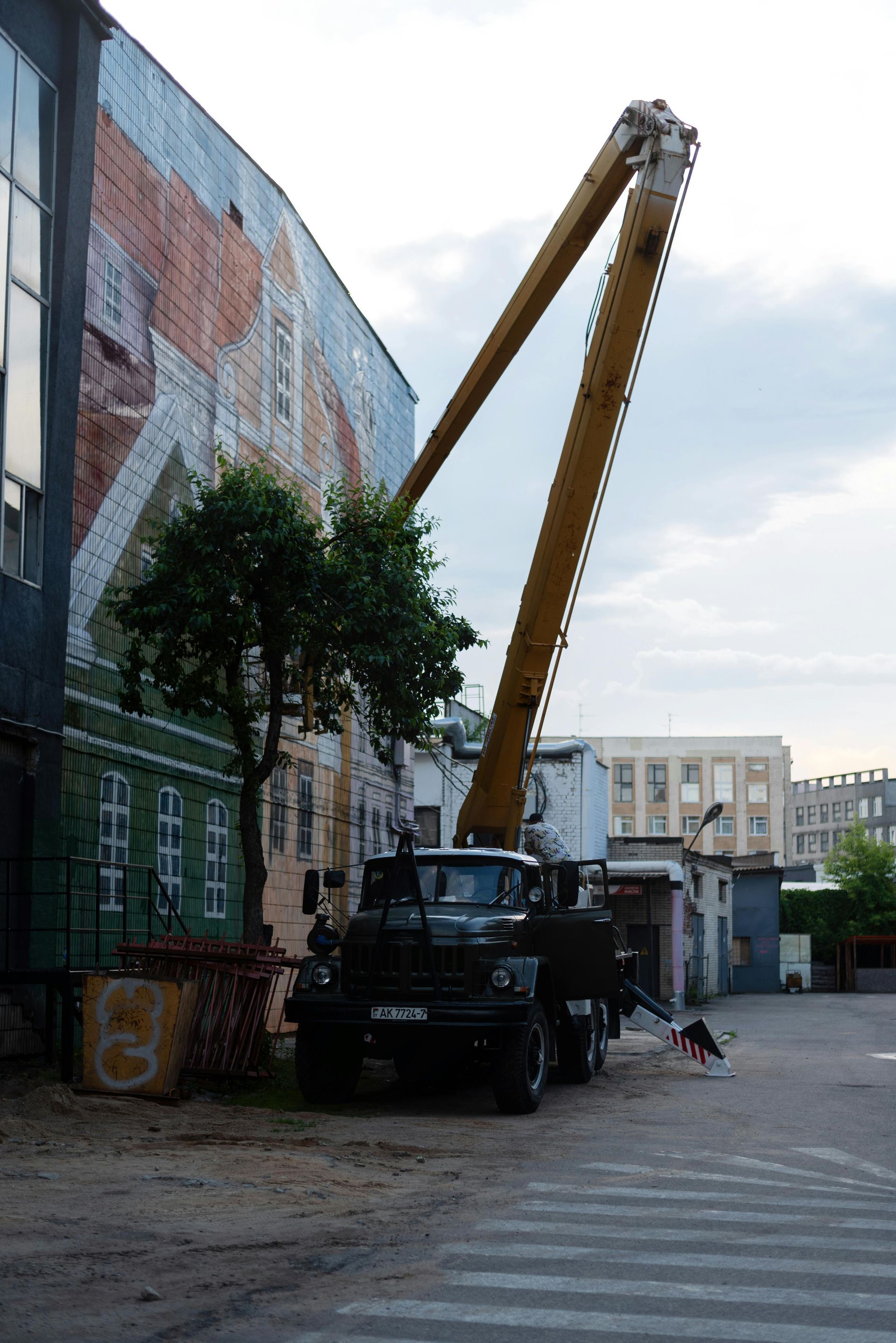 Truck with tall arm raised next to building with mural; dog walks in foreground.