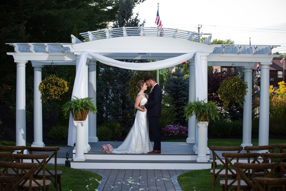 Couple embraces under a white gazebo at a wedding ceremony.