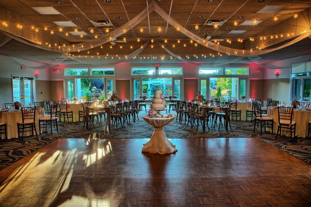 Wedding reception hall with tables, dance floor, cake, and string lights.