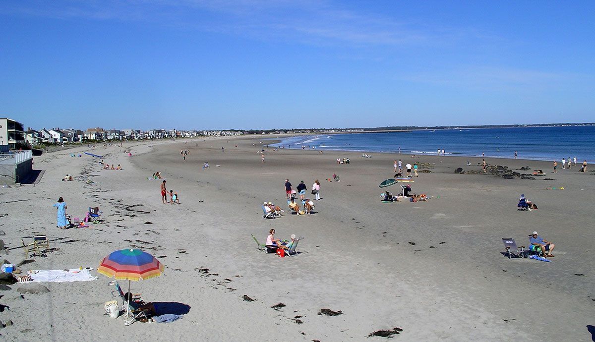 Beach scene with people, umbrellas, and a clear blue sky.