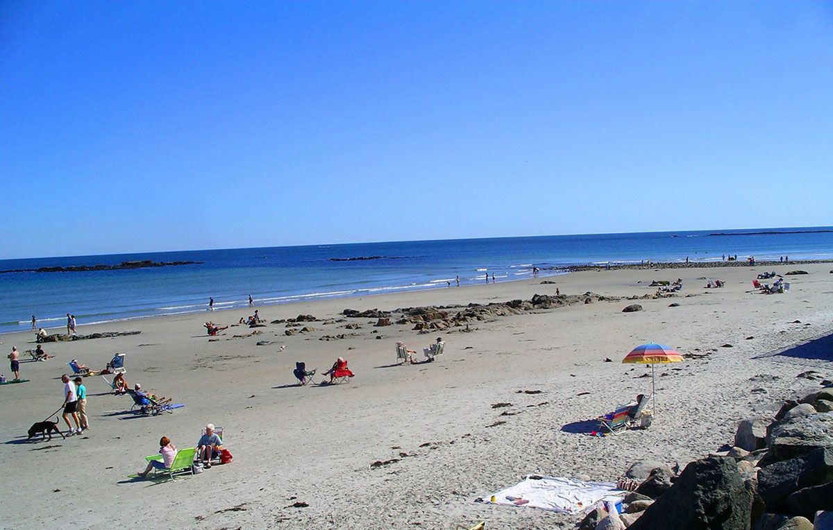 Beach scene with people relaxing, a clear blue sky, and the ocean.