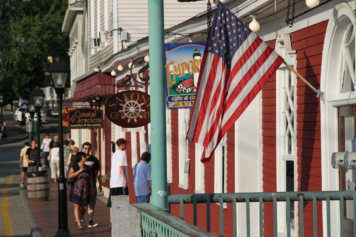 Street scene with shops, American flag, people walking. Red and white building.