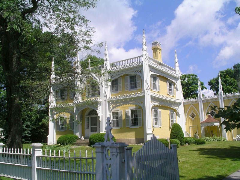 Yellow Gothic Revival house with white trim, picket fence, and green lawn.