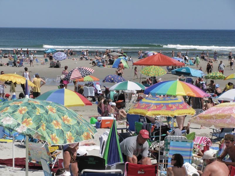 People relaxing on a sunny beach with colorful umbrellas, ocean in the background.