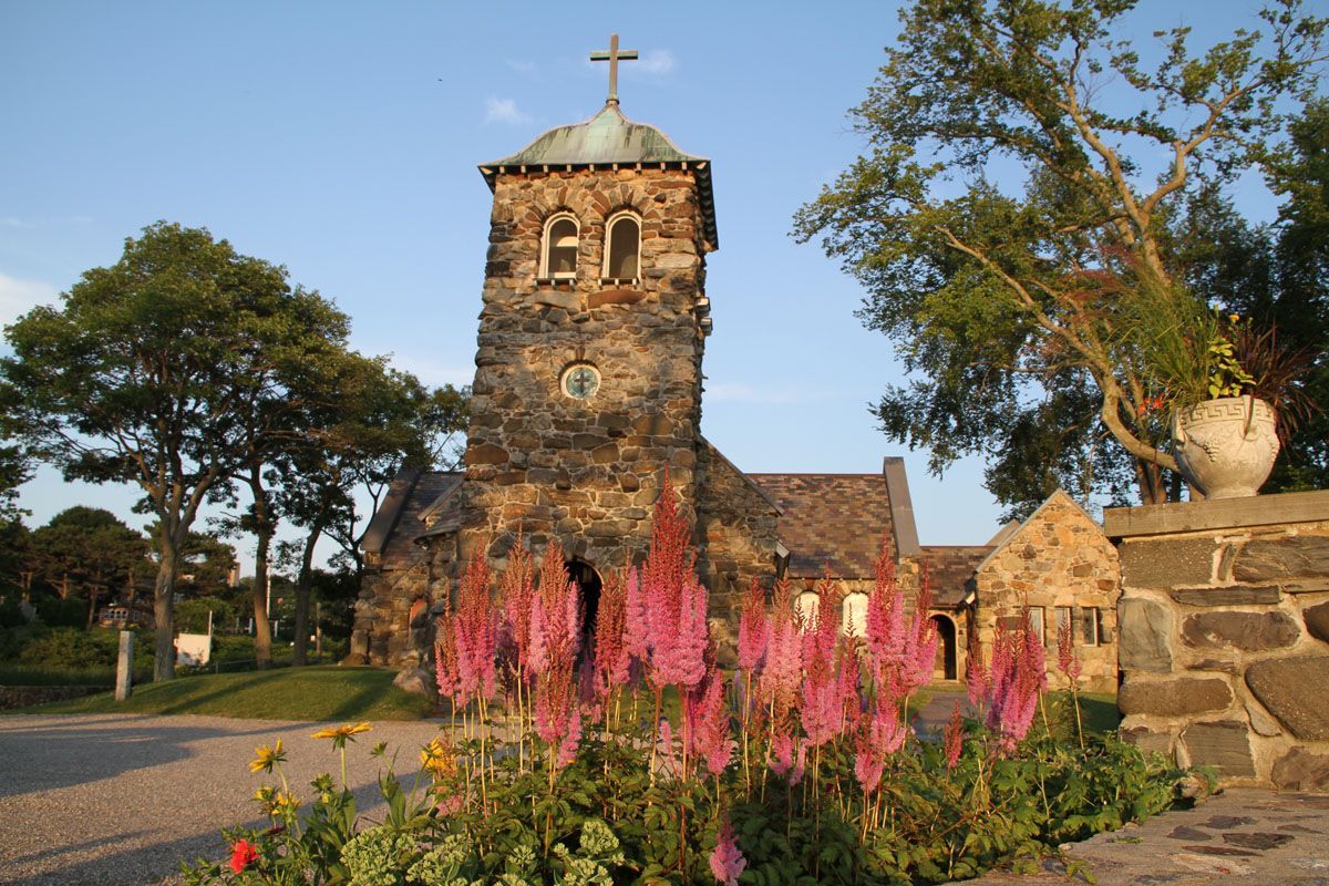 Stone church with tower, pink flowers, and a cross on top.