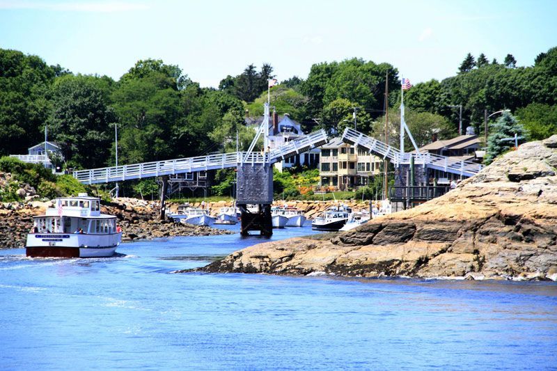 Boat passing through a drawbridge in a harbor, with buildings and green trees.