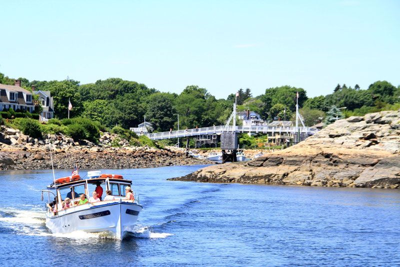 Boat in blue water, approaching a white bridge with a green tree-lined shore in the background.
