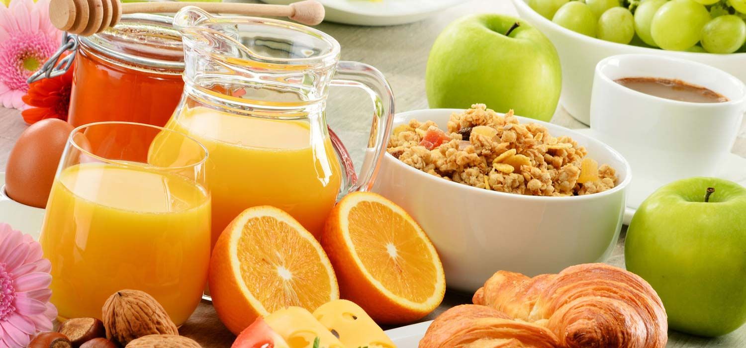 A spread of breakfast foods including fruit, juice, granola, and croissants.