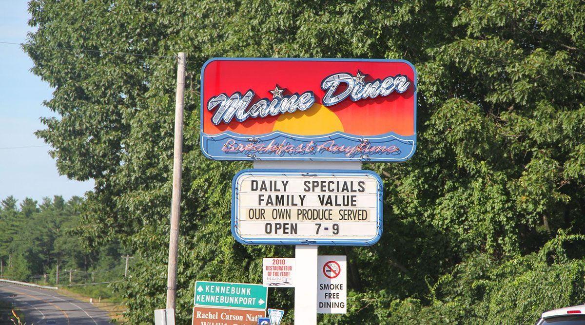 Maine Diner sign: red and blue with sunset graphic, white sign for daily specials, open 7-9.