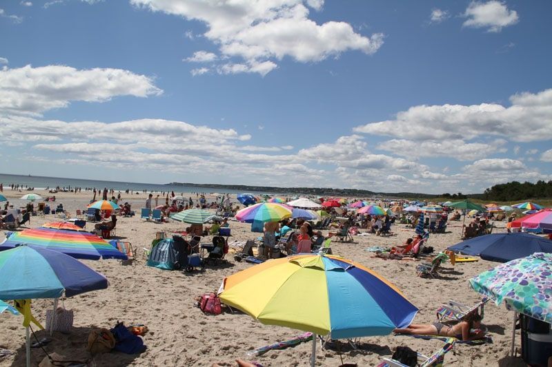 Beach scene with many colorful umbrellas, people sunbathing on a sunny day.