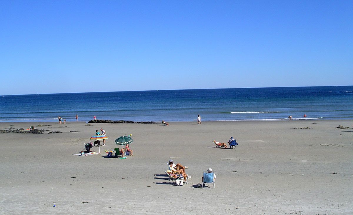 Sandy beach with people sunbathing, a clear blue sky, and the ocean in the background.