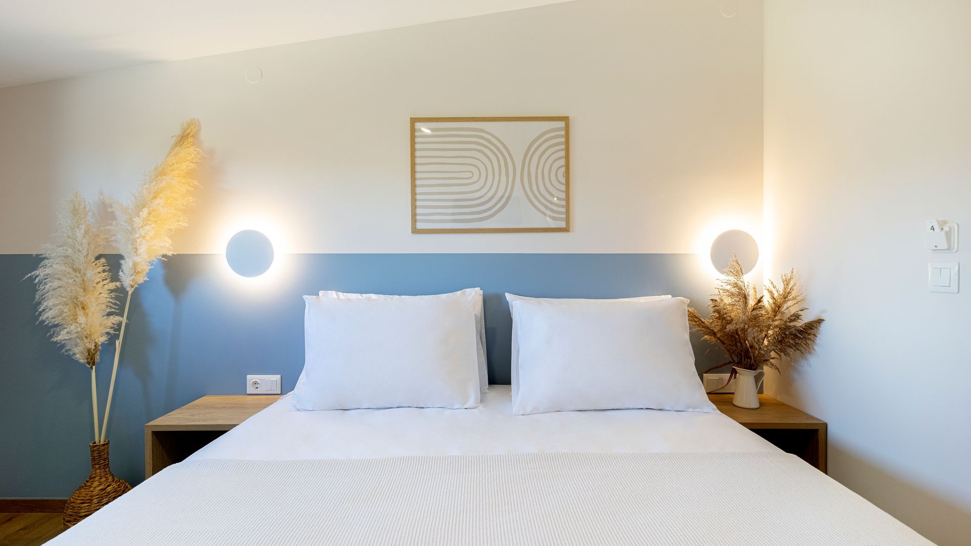 A bed with white sheets and pillows in a bedroom with a blue wall.