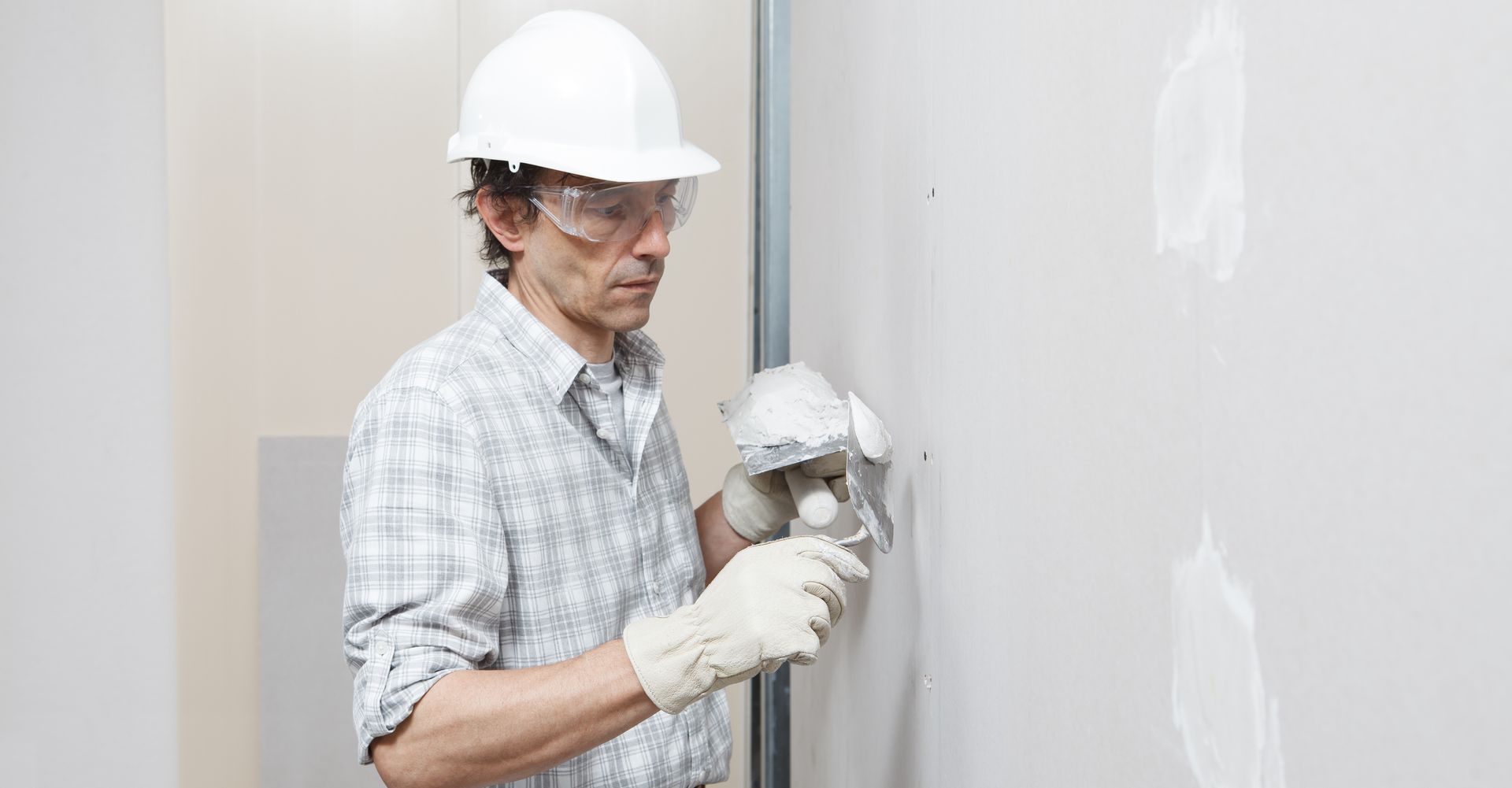 Construction worker in hard hat painting a wall with a roller, wearing safety goggles and gloves