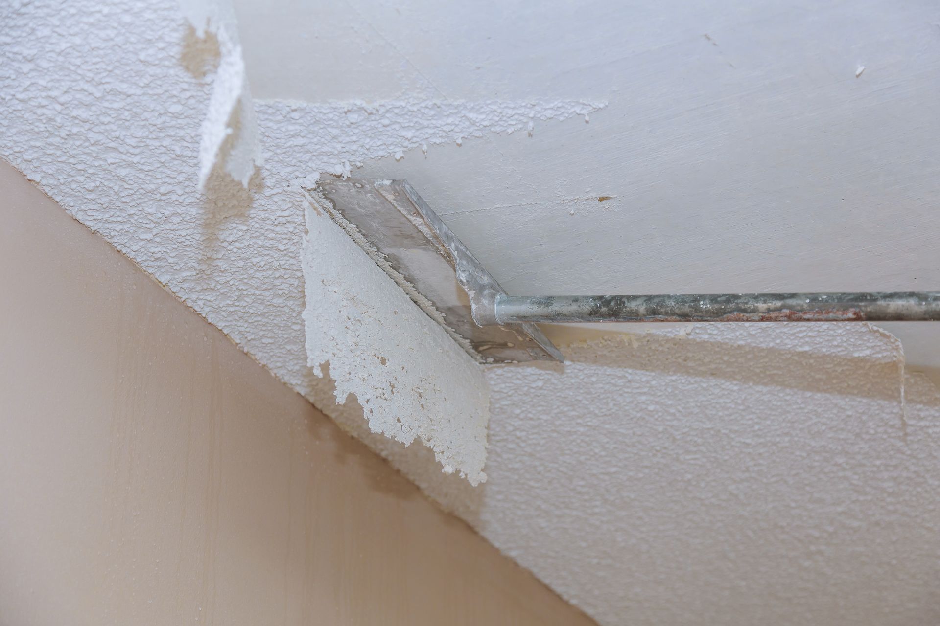 A person is peeling paint off of a wall with a spatula.