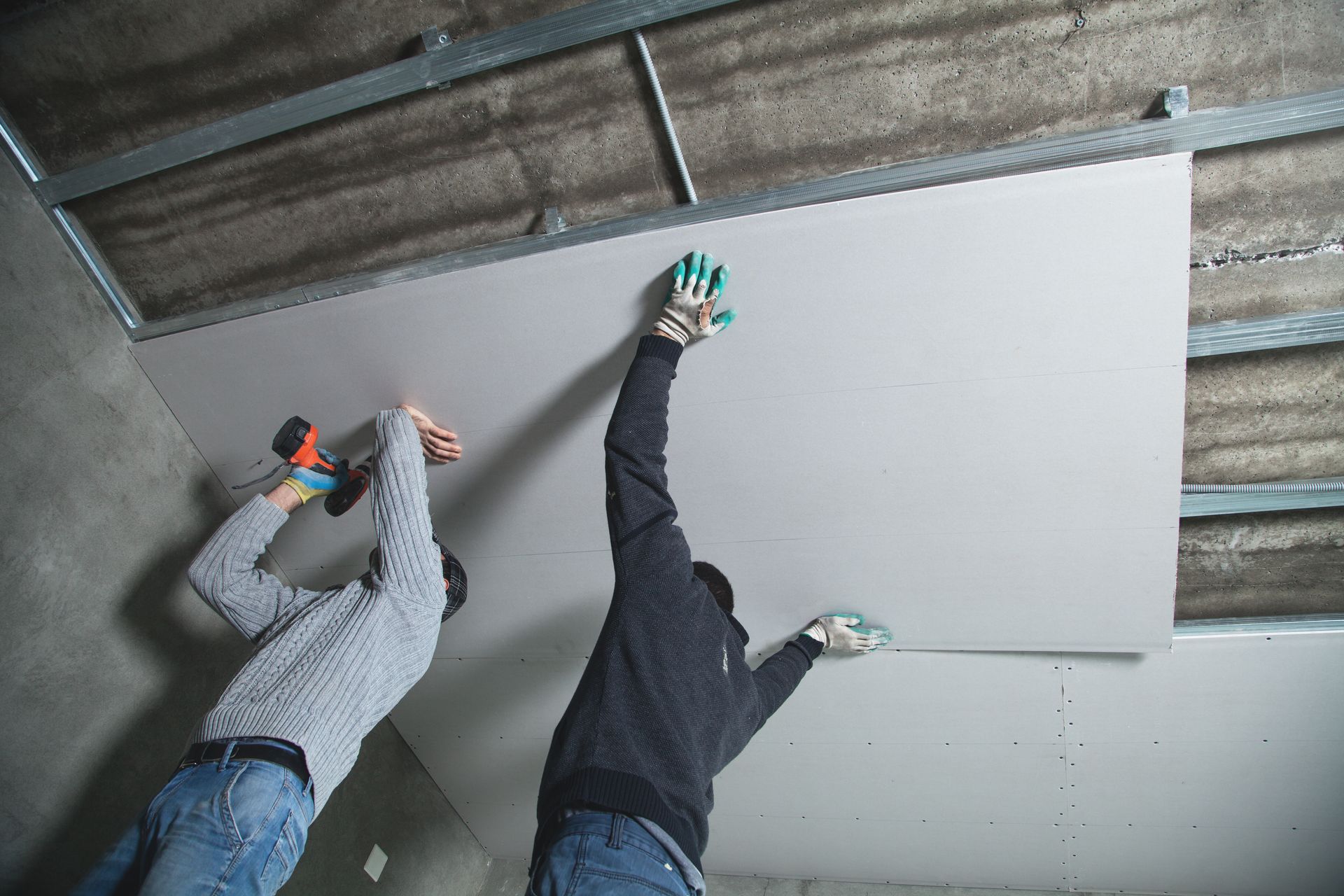 Two men are installing a drywall ceiling in a room.
