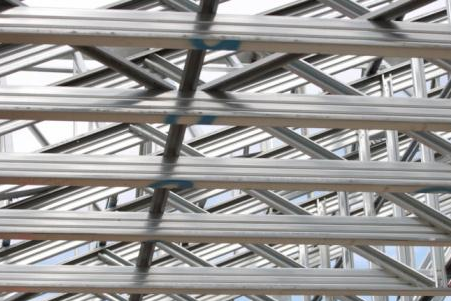 Estructura de acero del tejado de un edificio en construcción; vigas entrecruzadas contra un cielo parcialmente nublado.