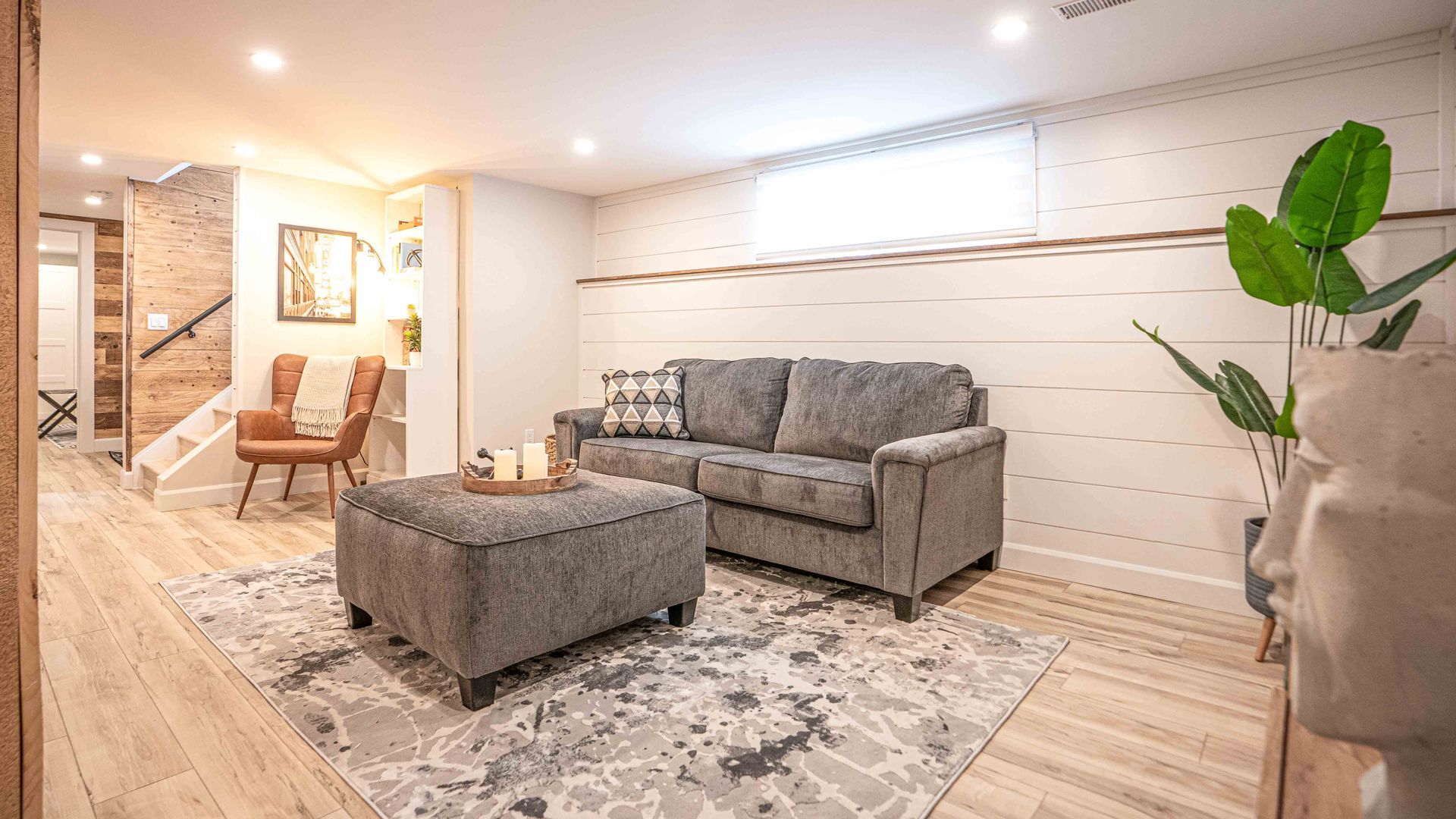 large living room, grey pullout couch with ottoman, brown leather chair in corner for reading with soft ambient warm light
