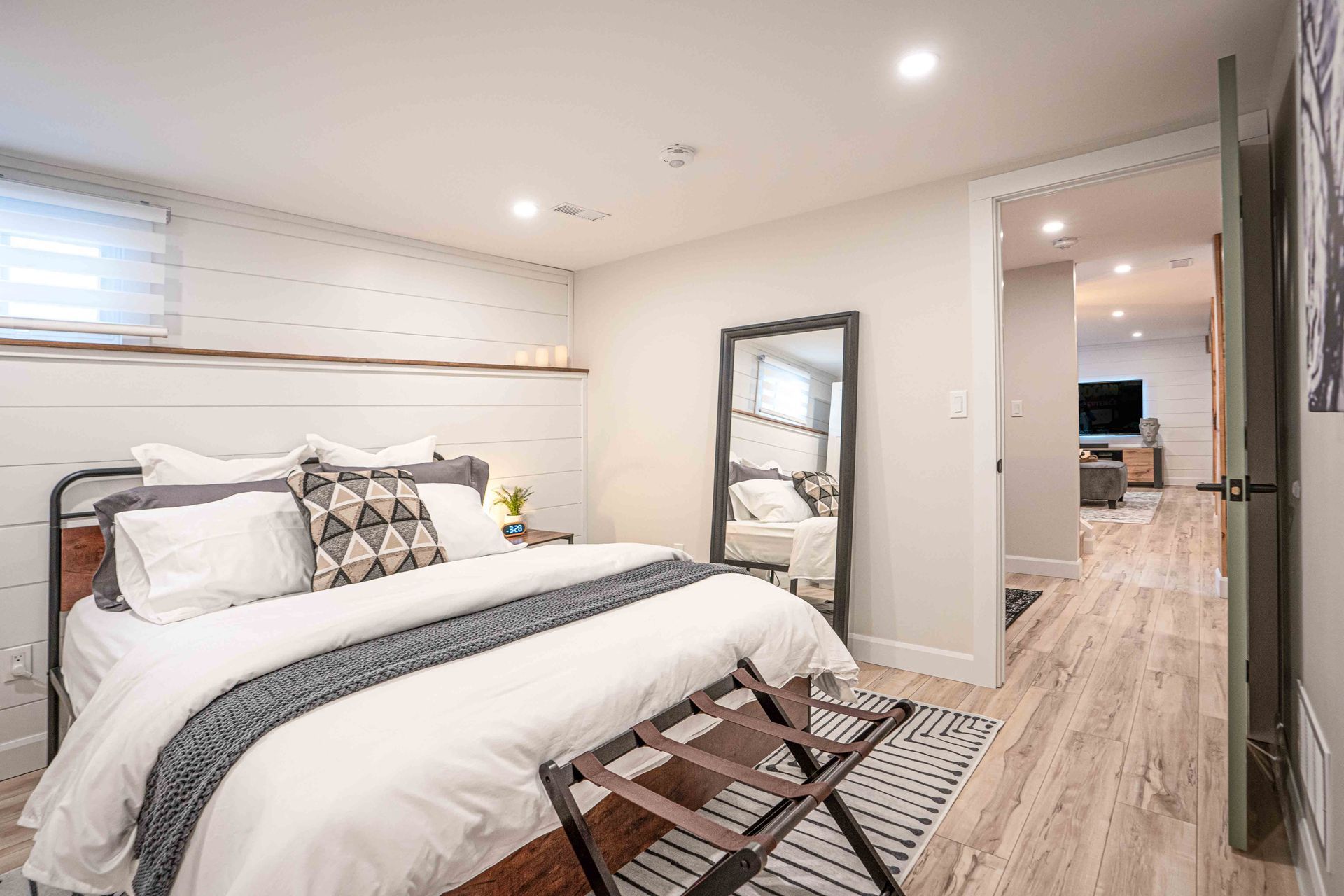 bedroom with a large bed in the foreground white walls with shiplap and a large mirror standing beside the bed door