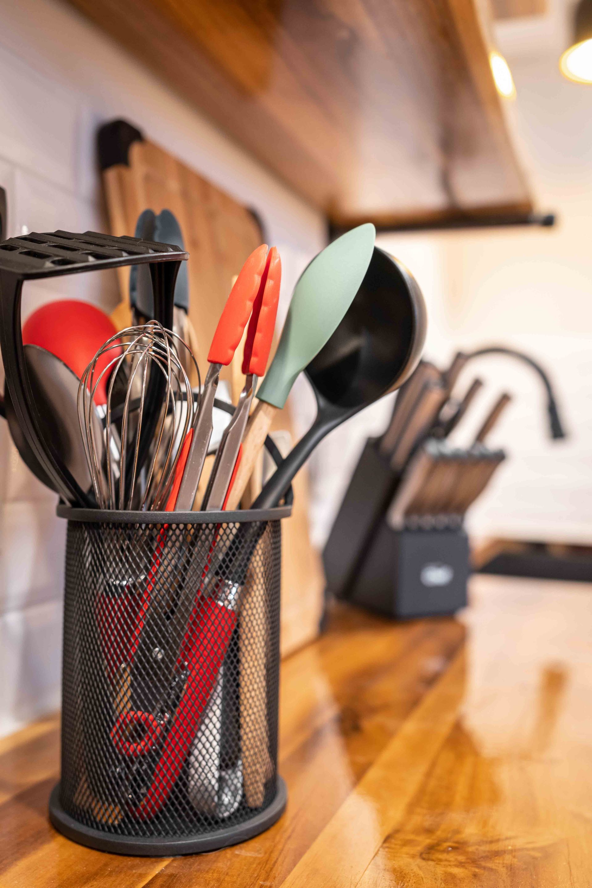 kitchen counter with a pot of kitchen utensils used for cooking like large spoons, a whisk, and tongs
