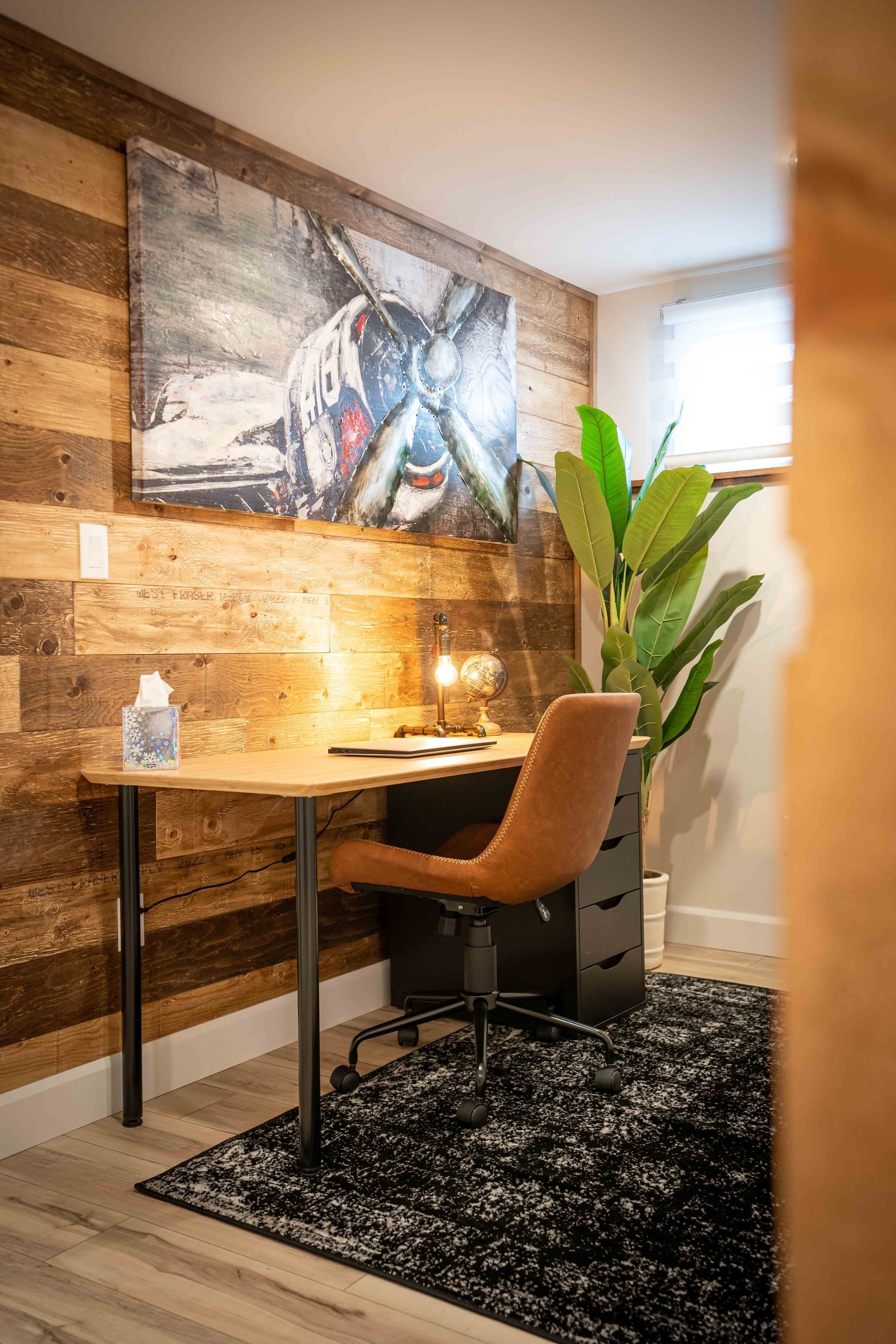 Home office with black desk and brown table top, picture of an old airplane, large green floor plant, brown leather chair