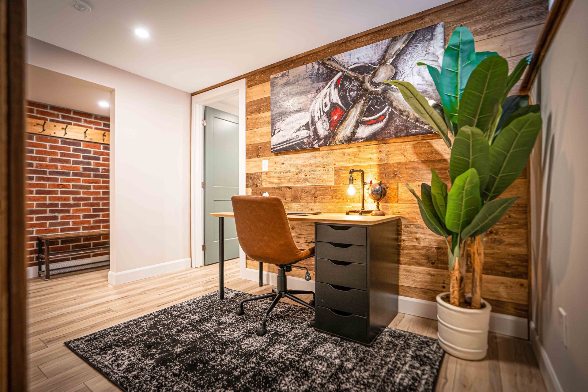 Office, desk area, with brown leather chair, large green floor plant, barn board walls, accent red brick wall
