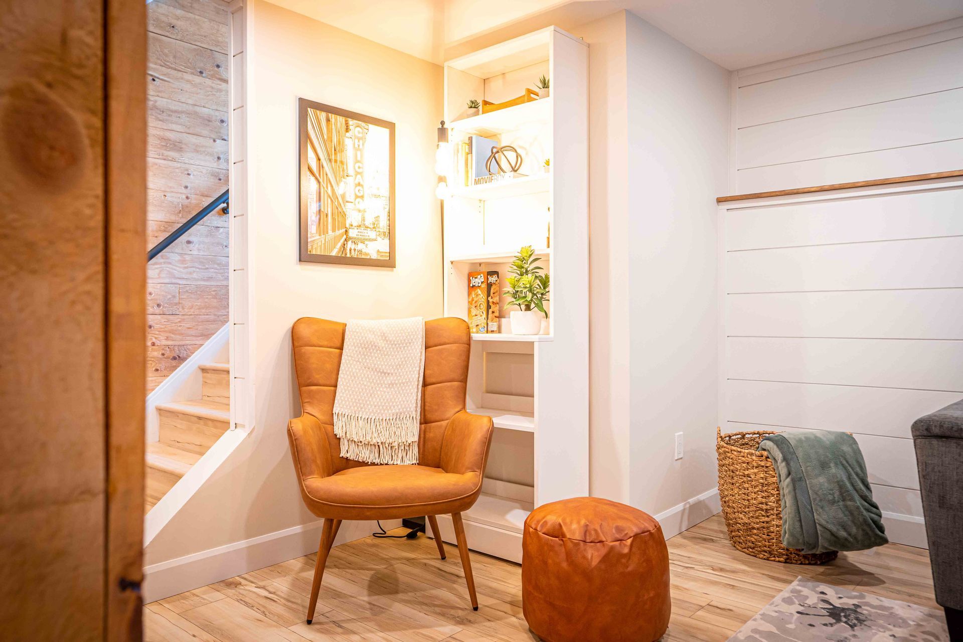 brown chair for reading, with bookshelf in the back, white shiplap walls, warm yellow light from floor lamp above chair
