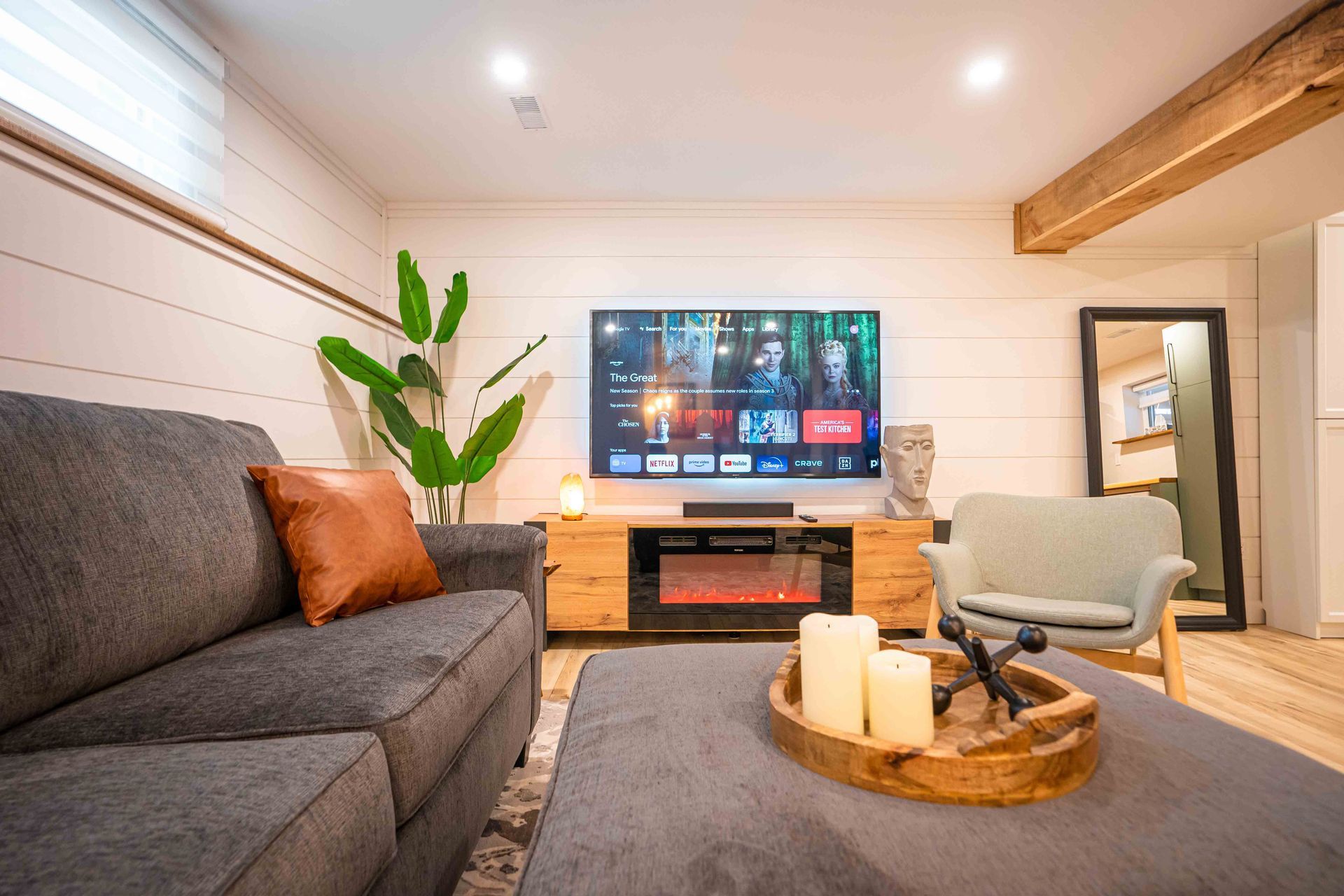 living room, with flatscreen tv on white shiplap wall, grey couch and large ottoman