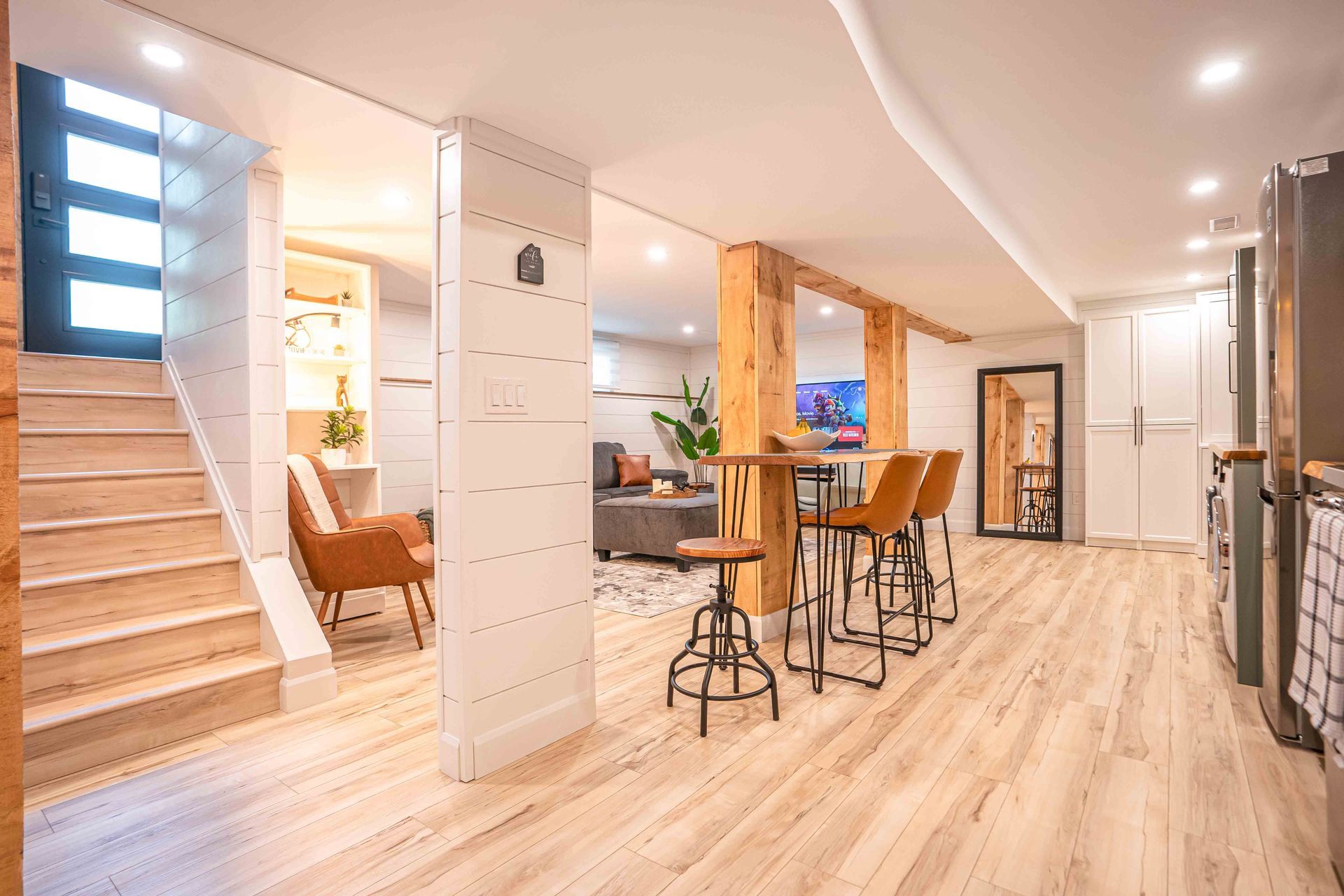 Entrance to unit, with light brown stairs coming from black door with windows, dining room table and chairs, wooden pillars 