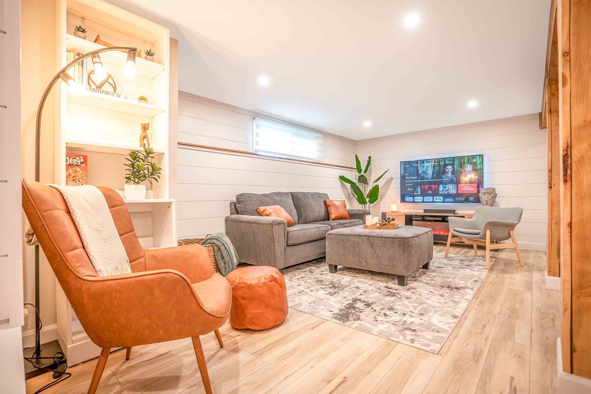 living room with brown reading chair, warm ambient light, grey couch and flat screen tv on wall
