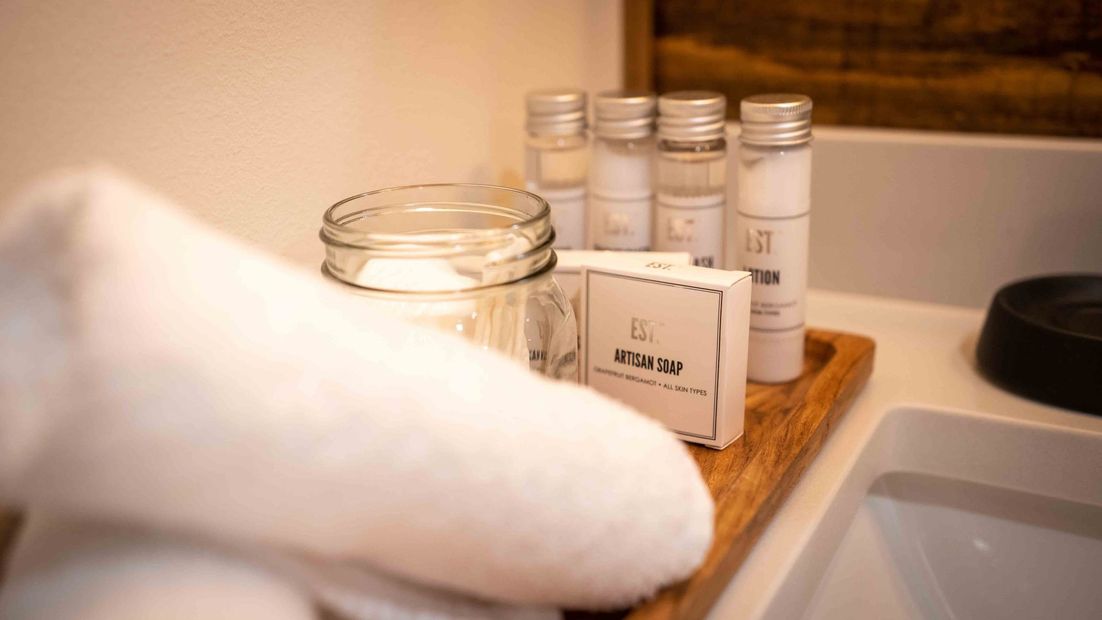 Bathroom amenities, with rolled up towels, a candle and small shampoo bottles