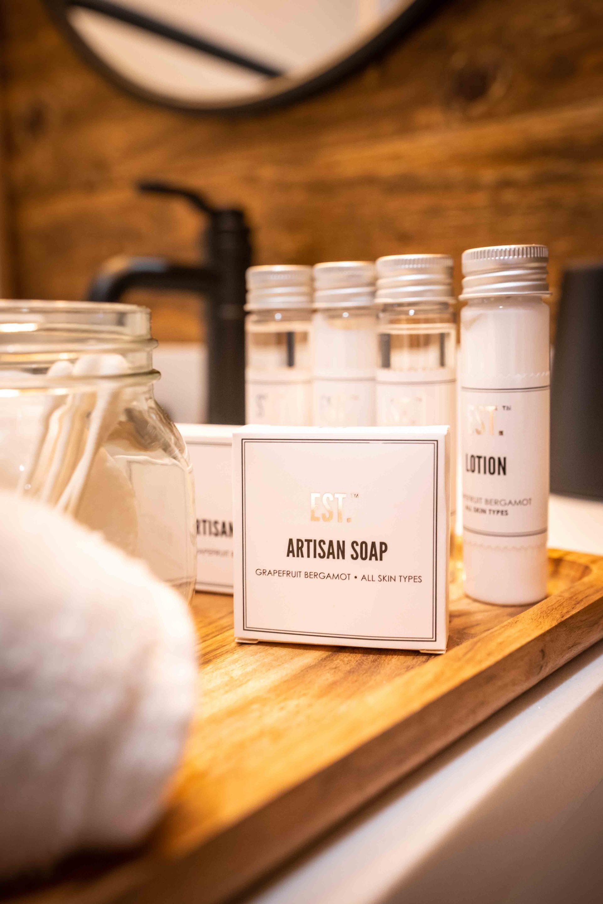 bathroom amenities with soaps in little jars on display with wooden background and the bathroom faucet in black
