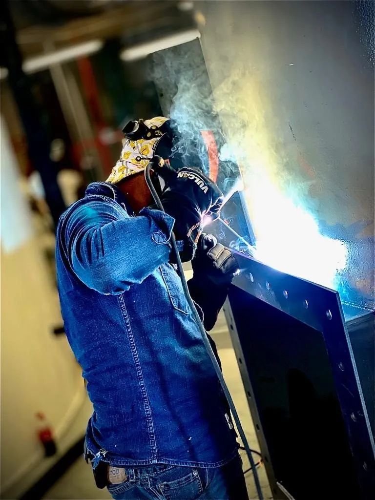 A man in a denim jacket is welding a piece of metal.