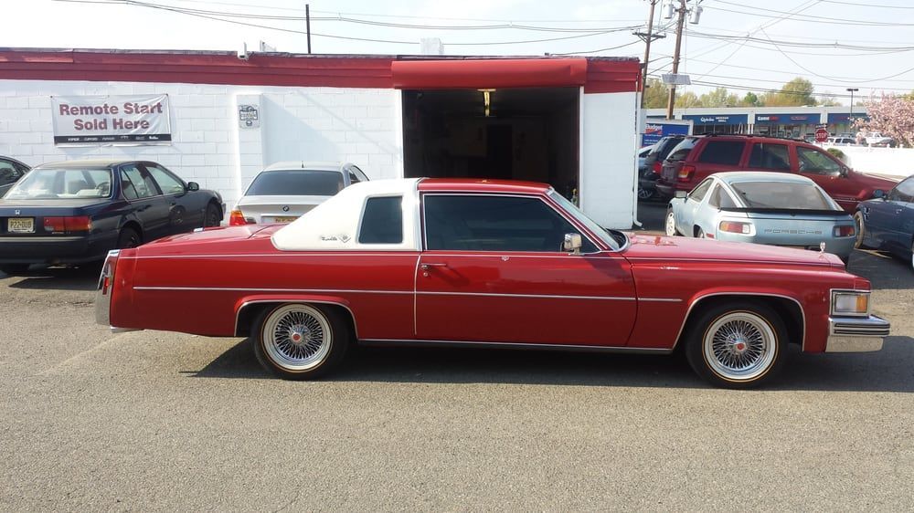 A red car with a white top is parked in front of a car dealership