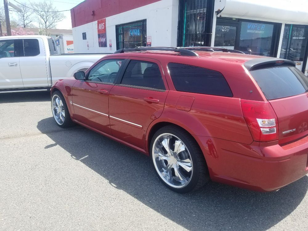 A red dodge magnum station wagon is parked in front of a white truck.