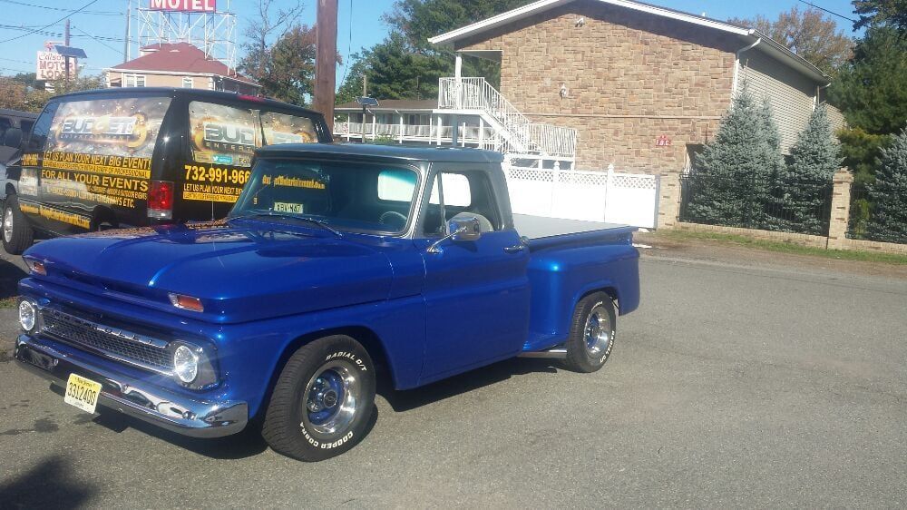 A blue truck with a white bed is parked in front of a motel.