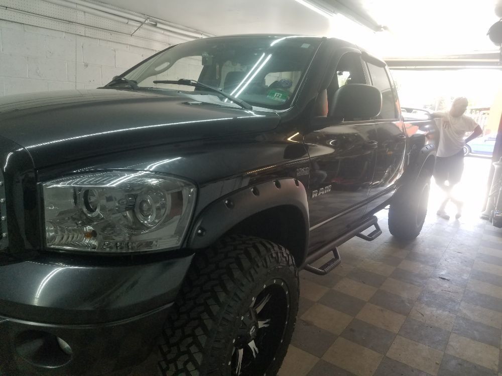 A black truck is parked in a garage with a man standing next to it.