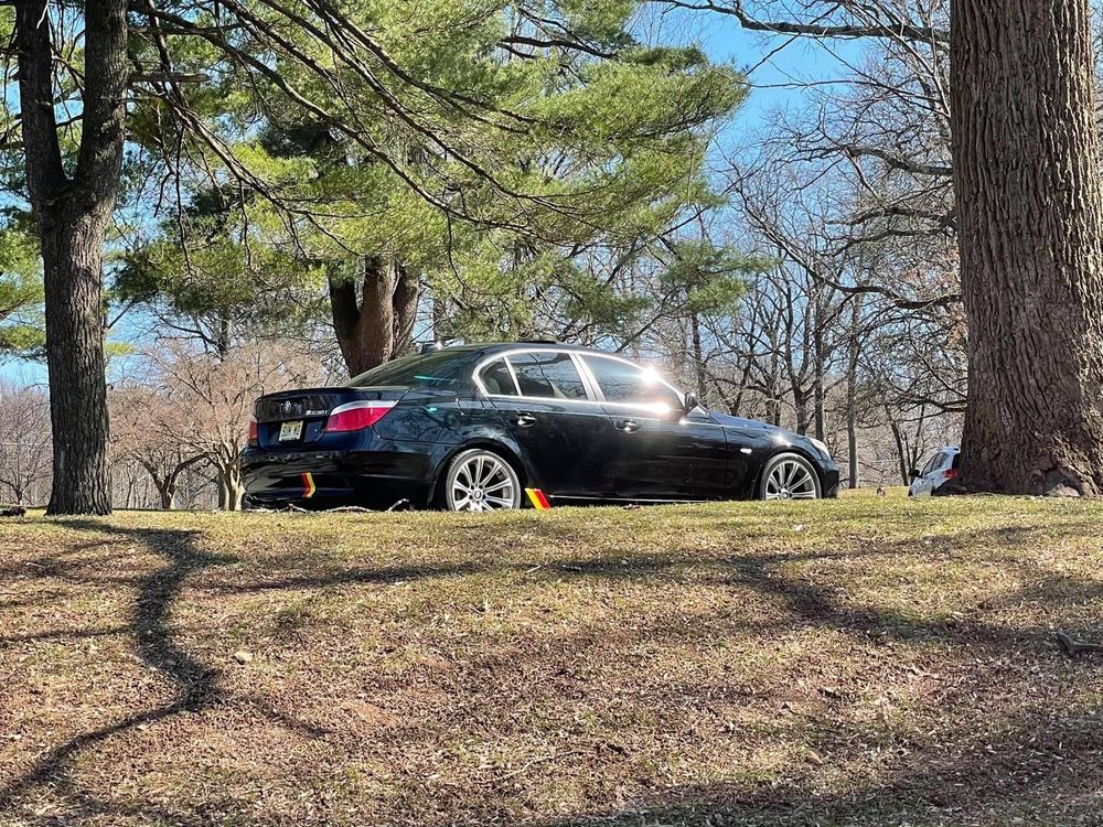 A black car is parked in a grassy field surrounded by trees.