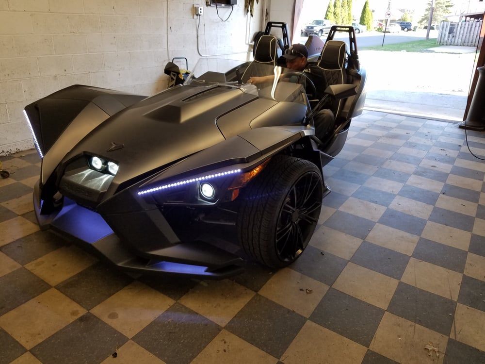A slingshot is parked in a garage with a checkered floor.