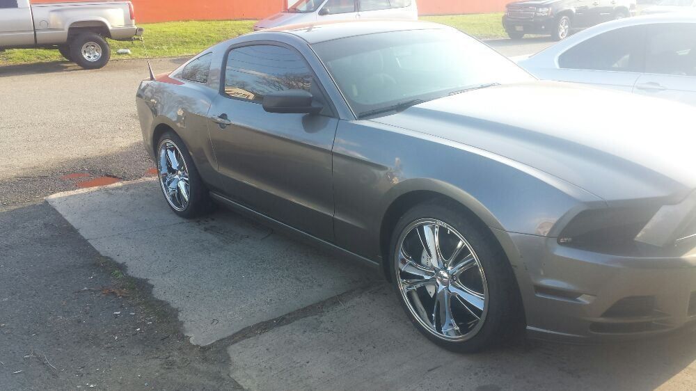 A gray mustang is parked in a parking lot next to a truck.